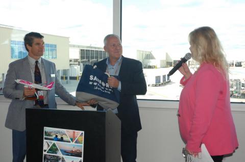 Orlando Sanford International Airport President and CEO Tom Nolan, left, and Shane Workman, center, head of Swoop Flight Operations, exchange gifts after the first flight to Sanford arrived Saturday morning. Elizabeth Brown of Orlando Sanford International Inc., greeted everyone Saturday.