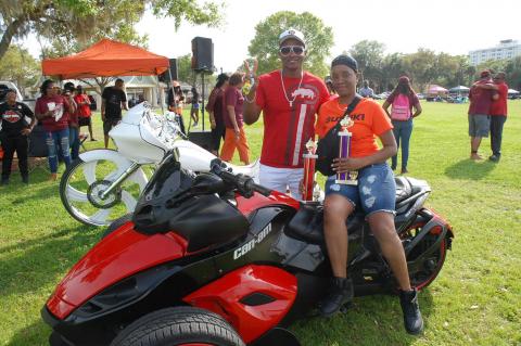 Kisha Williams holds both her trophy and Rico Sharp at the Bokey Riders Picnic in Fort Mellon Park Friday afternoon. Williams won best dressed motorcycle and Sharp had the best sound system.