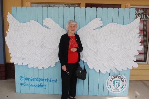In downtown for her 99th birthday Friday, Doris Duxbury of Sanford poses in front of the wings made from cutout music sheets in front of the Wayne Densch Performing Arts Center.