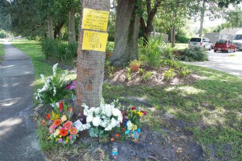 A memorial set up on Country Club Road has two signs, one which reads, “Please drive safe!”