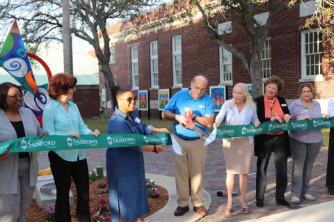CaSandra Williams (left), Rae Marie, Commissioner Sheena Rena Britton, Mayor Art Woodruff, Virginia Poe, Kimberly House, and Penny Szafran stand at the ribbon-cutting ceremony for the opening of the new Artisan Square next to the Sanford Information Center on Thursday. 
